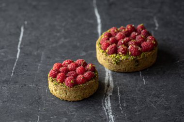 İki lezzetli ahududu turtası ve gri arka planda şam fıstığı