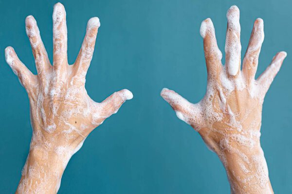 Two hands holded up with suds and soapy water in front of a blue background.