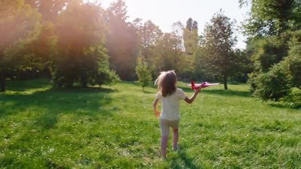 Пробіг маленького хлопчика з літаком через траву посеред парку в сонячний день — стокове відео