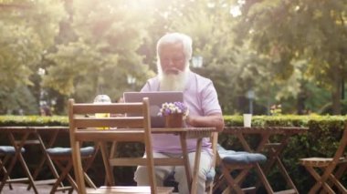 Parkın ortasındaki kafede oturan karizmatik yaşlı adam laptopuyla uyanıyor ve konsantre bir şeyler yazıyor.