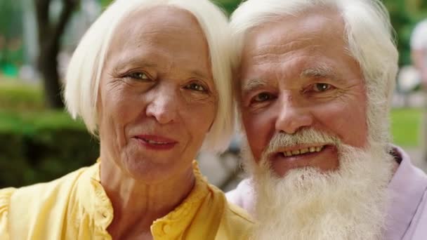 Delante de la cámara retrato de pareja de ancianos mirando directamente a la cámara y sonriendo a lo grande se abrazan — Vídeo de stock