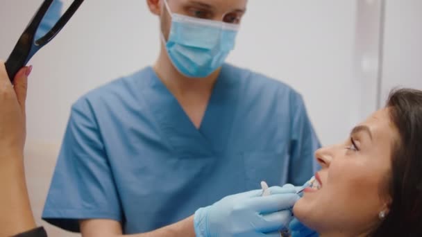 Dojrzała pacjentka z bliska ma wizytę u dentysty, który analizuje kolor zębów. — Wideo stockowe