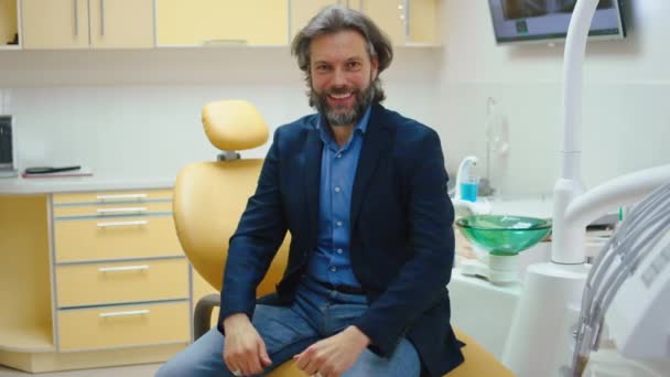 Перфектная улыбка пациента мужчина у стоматолога счастлив и взволнован после лечения полости рта он смотрит в камеру показывают свои идеальные зубы — стоковое видео