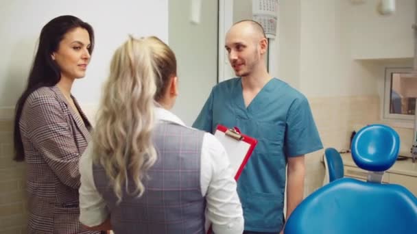 În clinica stomatologică modernă, un pacient drăguț vorbește cu asistentul dentar și medicul dentist care analizează rezultatele investigației — Videoclip de stoc