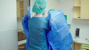 Ameliyathanede hemşire kadın cerrahi operasyona başlamadan önce doktora koruyucu üniforma giymesi için yardım ediyor.