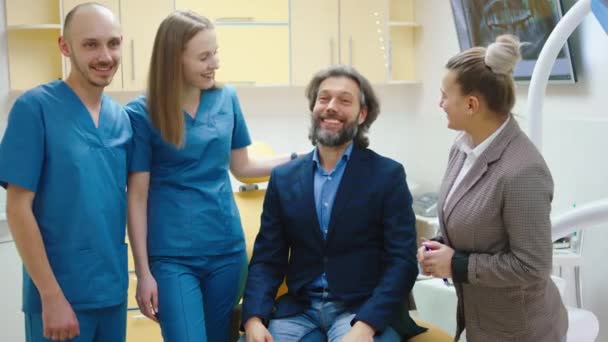 Equipo dentista feliz y emocionado en frente con el hombre paciente feliz mirando directamente a la cámara y disfrutar de los resultados de la atención oral — Vídeo de stock