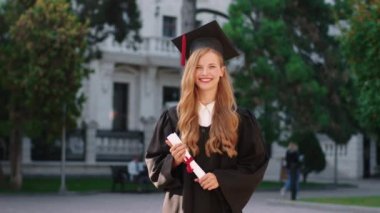 Mezuniyet günün kutlu olsun. Mezuniyet şapkası takmış, diplomasını tutarken kameranın önünde poz veren çok güzel bir genç kadın için. 4k