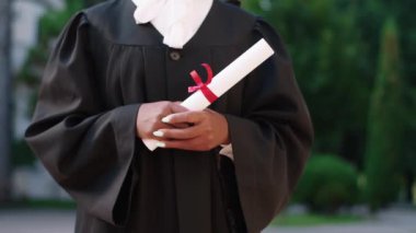 Güneşli bir günde diplomasını elinde tutan mezun bir bayan video detaylarını alıyor. 4k