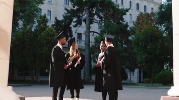 In een perfecte zonnige dag groep van multiraciale studenten na het afstuderen hebben een gesprek allemaal samen glimlachend en opgewonden ze houden diploma 's in handen. 4k — Stockvideo