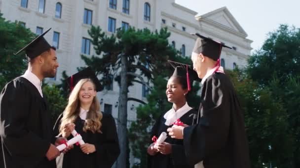 Pěkně vypadající skupina multietnických dam a chlapů v jejich maturitní den diskutovat a rychlost minule společně drží své diplomy fotit na památku — Stock video