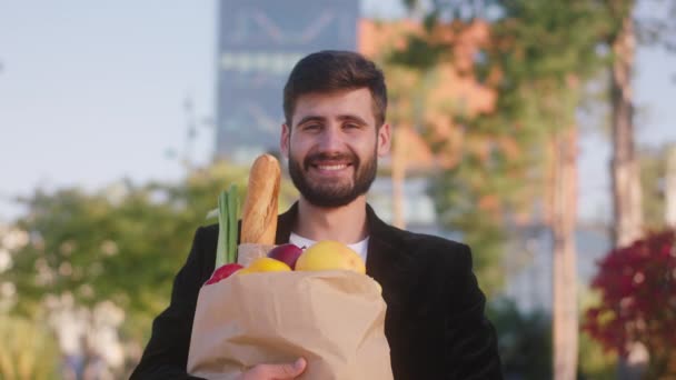 Elinde sebze ve meyve dolu bir çantayla caddenin ortasında kameraya bakan yakışıklı bir adamın yakın plan portresi. — Stok video
