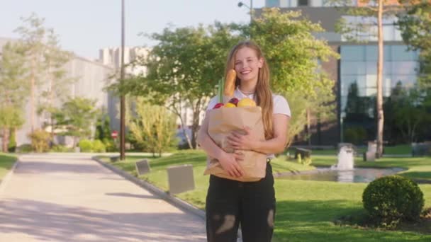 V slunečný den krásné blond vlasy žena uprostřed ulice pózuje před kamerou drží eko jídlo v tašce má dokonalý úsměv — Stock video