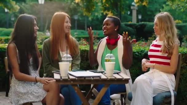 Güzel siyahi kadın ve parkın ortasındaki kafedeki diğer karizmatik bayanlar arkadaşça sohbet ediyorlar. — Stok video