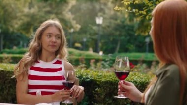 İnanılmaz derecede güzel bir sarışın kadın masada kızıl saçlı bir kadınla konuşuyor, etrafları ağaçlar, çalılar ve şarap kadehleriyle çevrili. 4k