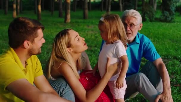 Hübsches kleines Mädchen und ihre Eltern zusammen mit Opa haben eine schöne Familienzeit zusammen in der Mitte des Parks genießen sie die gemeinsame Zeit — Stockvideo