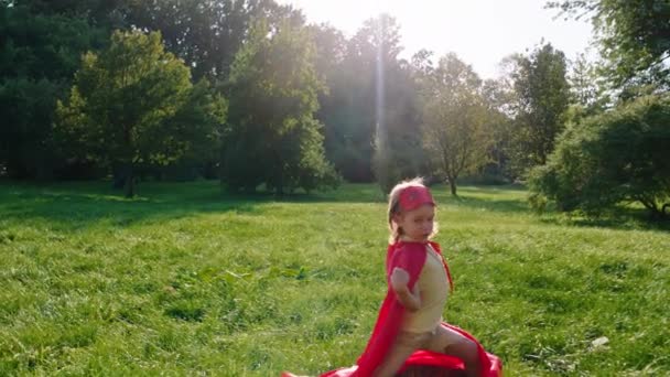 Charismatický roztomilý chlapec pózuje před kamerou velmi vzrušený v superhrdina oblek uprostřed parku přes trávu — Stock video