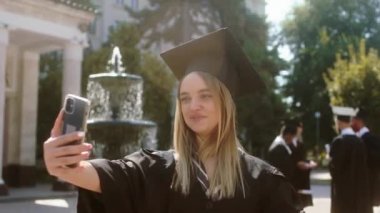 Üniversite bahçesinden mezun olan bayan mezun oldu. Ailesi için bir video çekmek için akıllı telefonu kullandı. Diplomasını ve meslektaşlarını gösterdi.