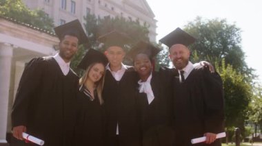 Modern üniversite bahçesi mezunları kameranın önünde heyecanlı pozlar vererek anılarını resmediyorlar.