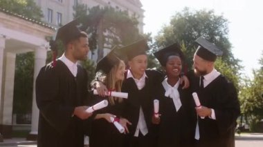 Yetişkin ve genç öğrencilerden oluşan mezuniyet günü grubu üniversite bahçesinde kameranın önünde bir araya gelip tartışıyorlar.