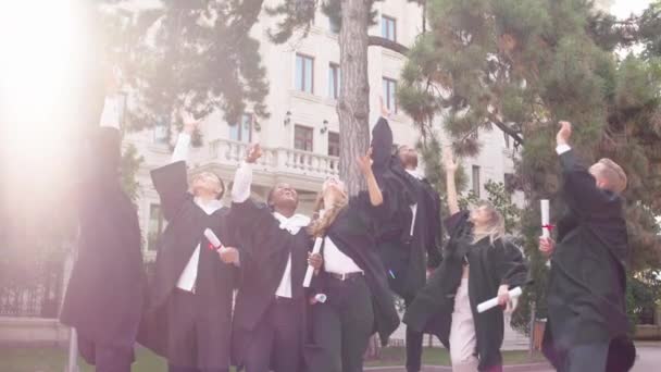 Grupo muito feliz e animado de senhoras e caras atraentes e bonitos após a formatura vomitar as tampas de formatura e abraçar animado todos juntos — Vídeo de Stock