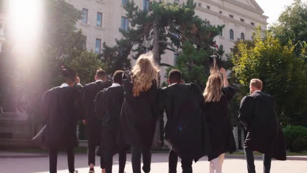 In the graduation day group of multiracial graduates students they walking in a group all together and throw up the graduation caps in the college garden. Shot on ARRI Alexa Mini. — Stock Video