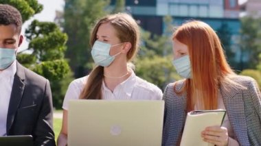 Karizmatik kadın ofis çalışanları ve bir siyahi adam, Coronavirus salgınında koruyucu maske takarak dizüstü bilgisayarlar ve tabletler üzerinde birlikte çalışıyorlar.