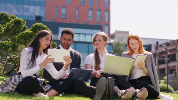 Office workers multiracial one guy and women team have a great day working in the business centre park down on the grass they take laptops and tablets to work together — Stock Video