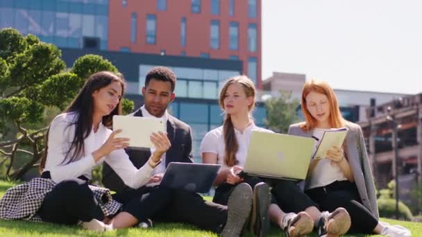 Les employés de bureau multiraciaux un homme et les femmes équipe ont une grande journée de travail dans le parc du centre d'affaires vers le bas sur l'herbe ils prennent des ordinateurs portables et des tablettes pour travailler ensemble — Video