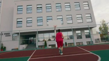 Büyük, modern bir stadyumda basketbol oynayan yakışıklı bir adam basketbolu sepete atar.