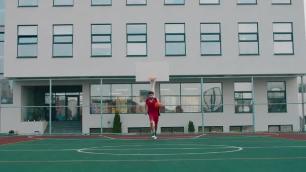 Μοντέρνο μεγάλο γήπεδο μπάσκετ όμορφος άντρας παίζει μπάσκετ μπροστά στην κάμερα συγκεντρωμένος τρέχει πίσω από την μπάλα — Αρχείο Βίντεο