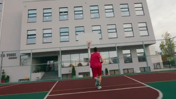 Na dużym, nowoczesnym stadionie przystojny mężczyzna gra w koszykówkę i rzuca piłkę do kosza. — Wideo stockowe