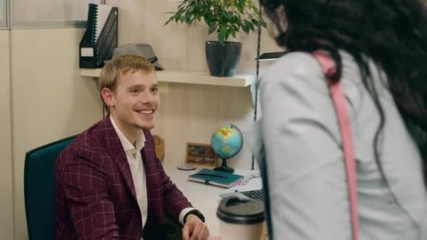 Милий офіс-менеджер чоловік на своєму робочому місці в офісі розмовляє зі своєю помічницею в офісі, вона приносить каву і дає один менеджеру — стокове відео