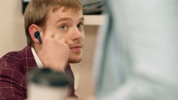 En el centro de negocios oficinista toma el café de su colega y sonriendo a lo grande tiene auriculares. 4k — Vídeos de Stock