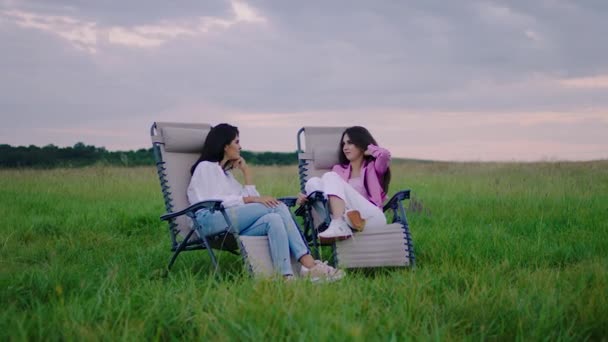 Посеред великого поля на стільцях сидять дві привабливі жінки, які обговорюють щось разом дуже концентроване і захоплююче — стокове відео