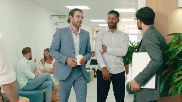 一名身穿蓝色西服的男子走进大厅，与正在交谈的两名工人会合，两名职业女性从这三名男子旁边走过。4k — 图库视频影像