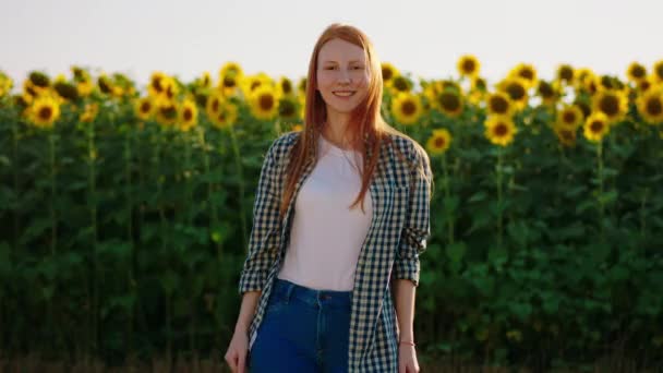 Een jonge foxy uitziende vrouw draagt een geruite blouse en staat voor een zonnebloemenveld met haar duimen omhoog terwijl ze glimlacht op grote schaal naar de camera — Stockvideo