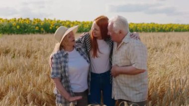 Kameranın önünde yakışıklı yeğen ve büyükannesi ve büyükbabası buğday tarlası aile tarımı konseptinde birbirlerine sevgiyle sarılıyorlar. 4k
