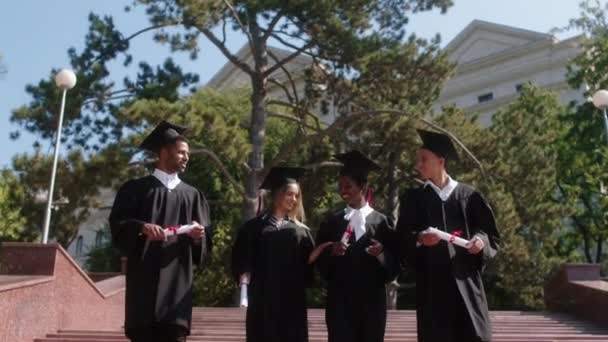 W nowoczesnym ogrodzie kolegium grupa studentów wielorasowych absolwentów schodzących po schodach trzymając dyplomy w rękach. Strzał na ARRI Alexa Mini. — Wideo stockowe