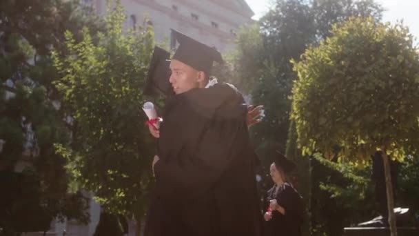 Mezun olan çok ırklı erkek ve genç kadın, mezuniyetten sonra birlikte tartıştıkları ve diplomalarını ellerinde tuttukları üniversite bahçesinde mutlu ve heyecanlı bir şekilde birbirlerine sarılıyorlar. — Stok video