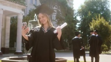 Güzel, genç bir kız öğrenci, üniversite bahçesinde diplomasını tutarken çok heyecanlı olduğunu tartıştığı akıllı telefonu kullanarak ailesini kameradan aradı.