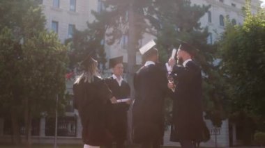 Mezuniyet kıyafetleri ve şapkalar giyen bir grup öğrenci için harika bir gün. Diplomaları aldıktan sonra dans ediyorlar ve heyecanlanıyorlar.