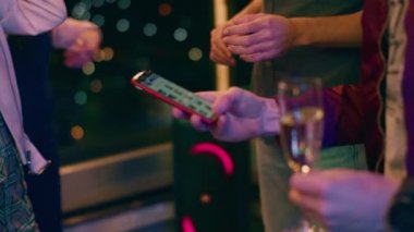 Kameraya yaklaş. Partide elinde akıllı telefonu olan bir adam elinde tuttuğu hoparlöre müzik ve bir bardak şampanya koydu.
