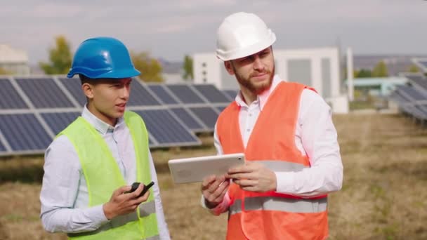 Ein Industriemechaniker und Öko-Ingenieur mit Schutzhelmen und digitalem Tablet zur Steuerung der Photovoltaik-Batterien — Stockvideo