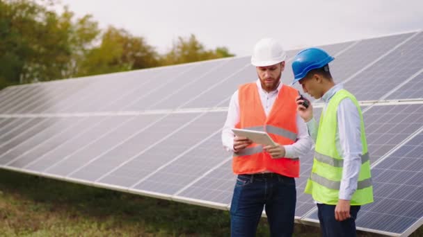 Перед камерой харизматичные многорасовые экологические инженеры обсуждают возможность управления фотоэлектрическими батареями на современной солнечной электростанции — стоковое видео