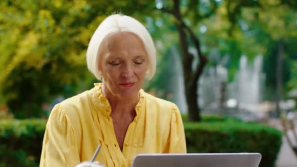 一位迷人的老妇人在公园中央的咖啡店里工作，专心致志地在笔记本电脑上打字。向ARRI Alexa Mini开枪. — 图库视频影像
