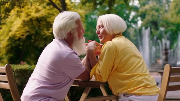 Sehr attraktives altes Paar mit einem breiten Lächeln im Café führt ein romantisches und schönes Gespräch, während es sich die Hände umarmt — Stockvideo