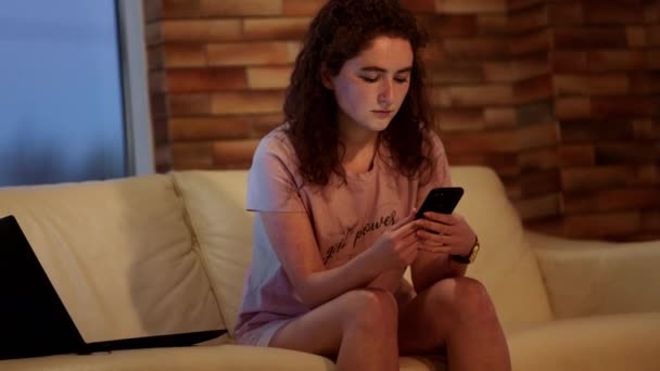 Snygg dam i vardagsrummet arbetar hårt på sin bärbara dator och smartphone på samma gång hon är koncentrerad. 4k — Stockvideo