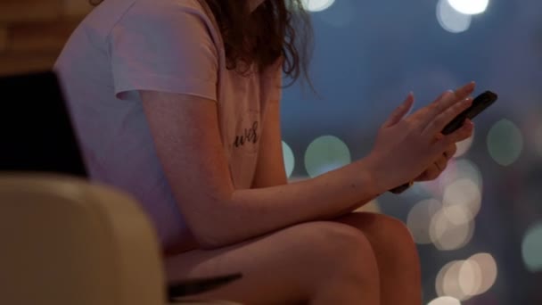 Concentrada adolescente senhora com um rosto triste mensagens de texto algo em seu smartphone enquanto sentado no sofá na sala de estar — Vídeo de Stock