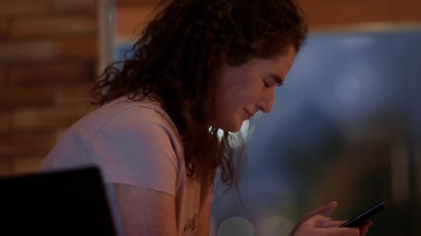Belle adolescente qui pleure tout en envoyant un message sur son smartphone elle est assise dans le salon sur le canapé — Video
