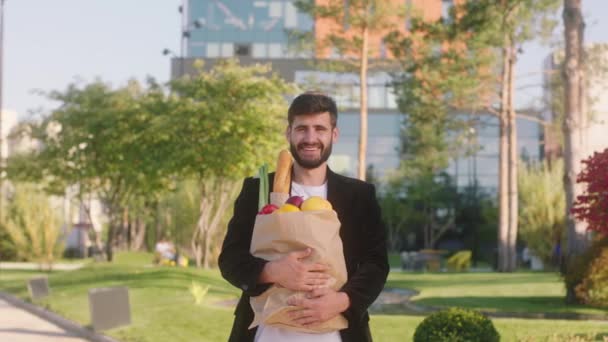 Homem atraente após loja posando feliz com um saco ecológico cheio de comida ele está em frente à câmera no meio da rua moderna — Vídeo de Stock